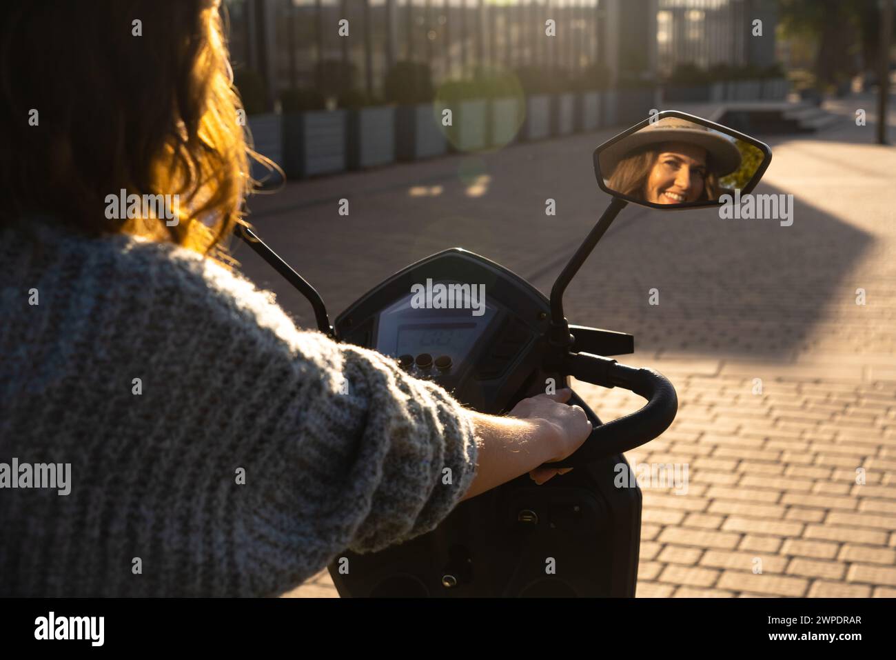Frau Tourist auf einem Elektroroller mit vier Rädern auf einer Stadtstraße. Das Gesicht der Frau ist im Rückspiegel sichtbar. Stockfoto