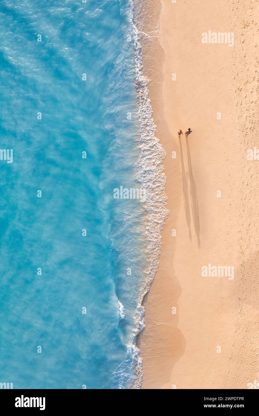 Romantischer Blick aus der Vogelperspektive auf ein Paar, das am Sonnenstrand spazieren geht, lange Schatten, idyllische Sommerurlaub-Abenteuer-Stimmung. Outdoor Freizeitaktivitäten Top Drohne Stockfoto