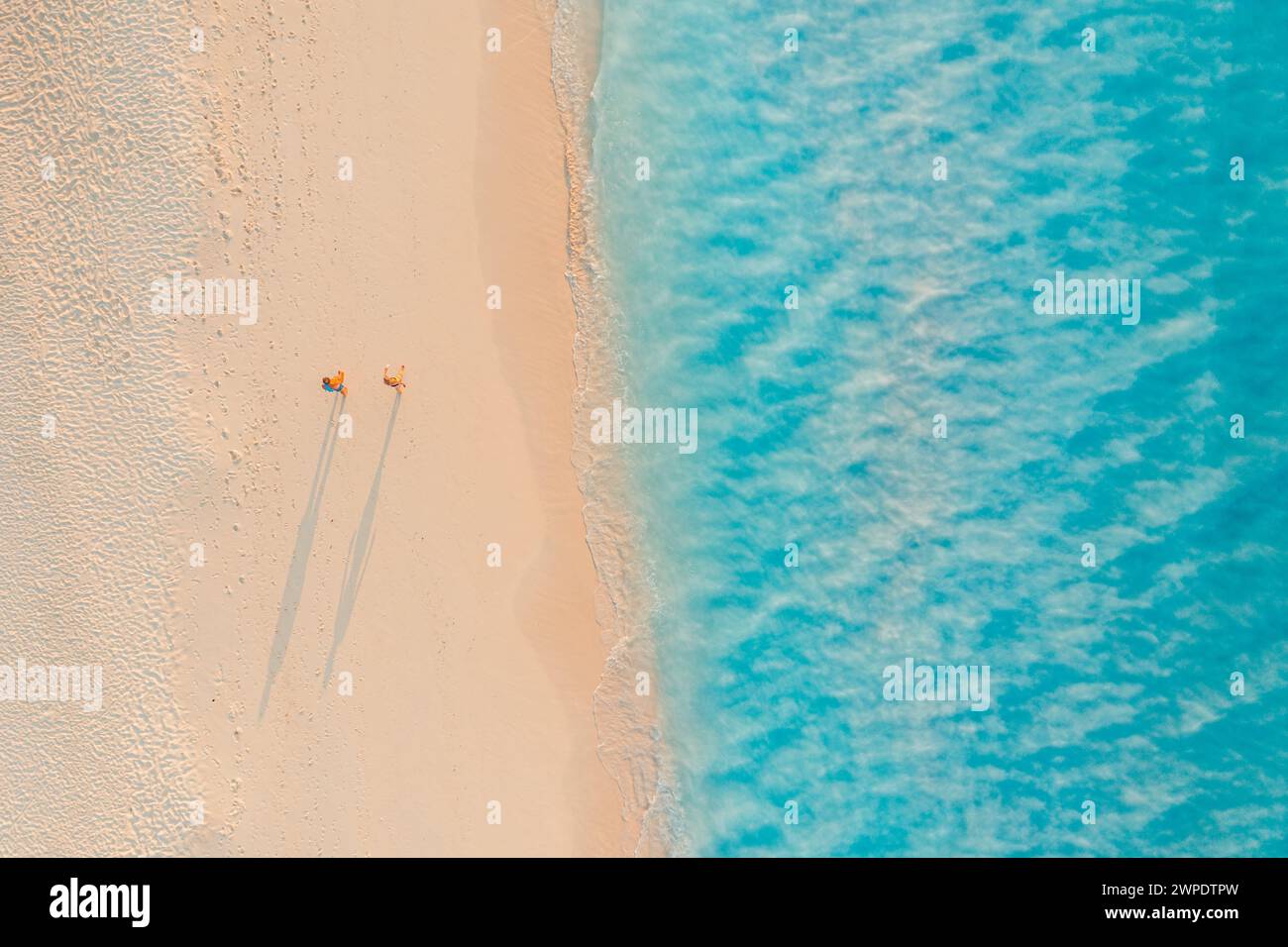 Romantischer Blick aus der Vogelperspektive auf ein Paar, das am Sonnenstrand spazieren geht, lange Schatten, idyllische Sommerurlaub-Abenteuer-Stimmung. Outdoor Freizeitaktivitäten Top Drohne Stockfoto