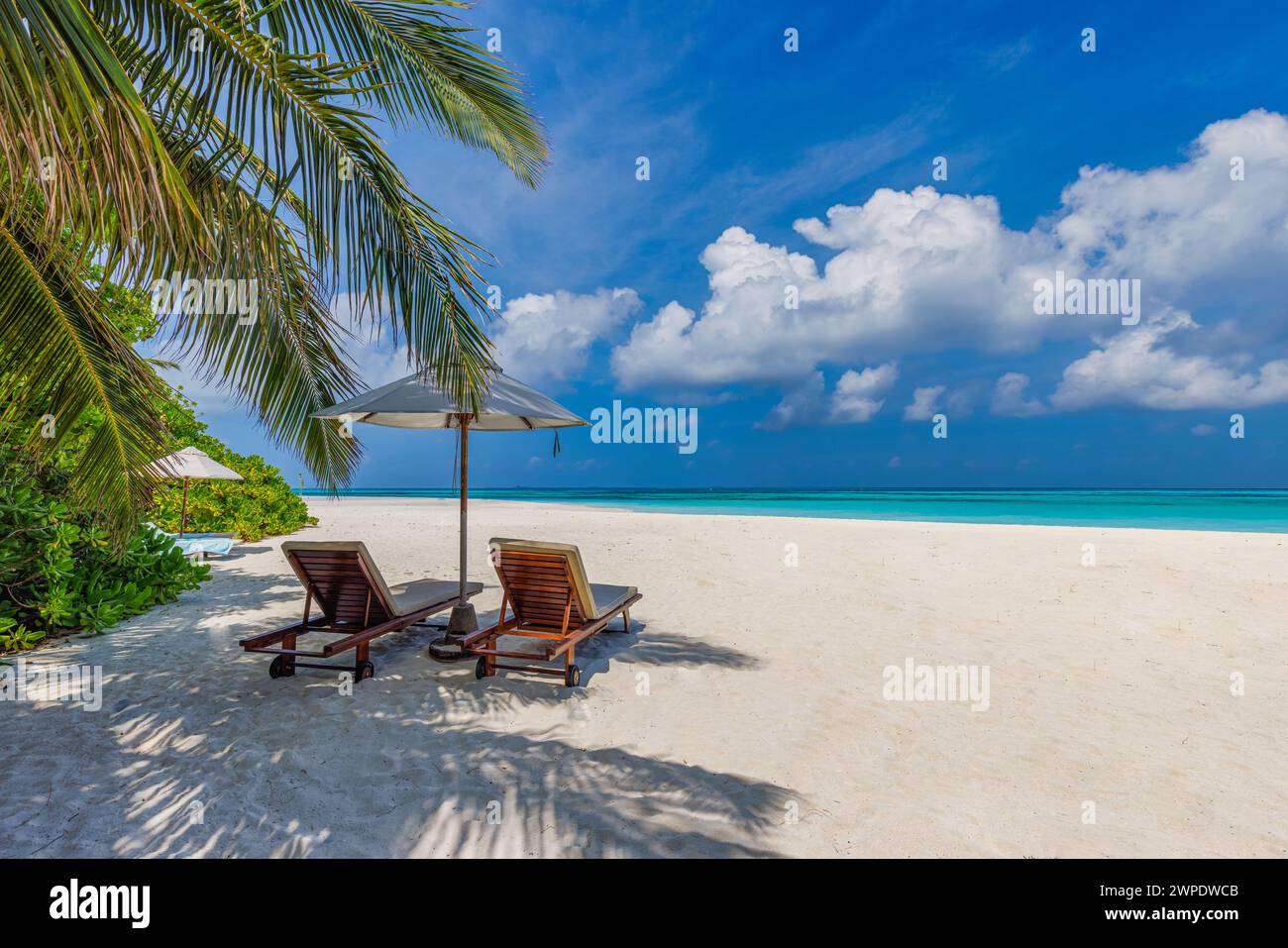 Tropischer Strand, Hintergrund mit Sommerlandschaft mit Liegestühlen, Palmen, ruhigem Meer, Sandhimmel. Romantischer Flitterwochentourismus. Liebe Zweisamkeit Stockfoto
