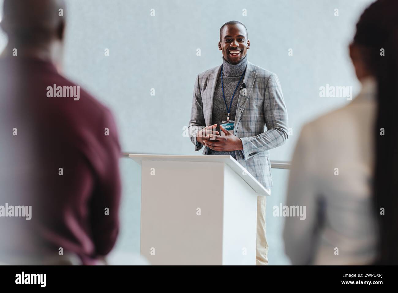 Ein professioneller Geschäftsmann mit einem warmen Lächeln spricht ein Publikum während einer Unternehmenspräsentation an. Interaktion mit dem Publikum und effektive Kommunikation in A Stockfoto