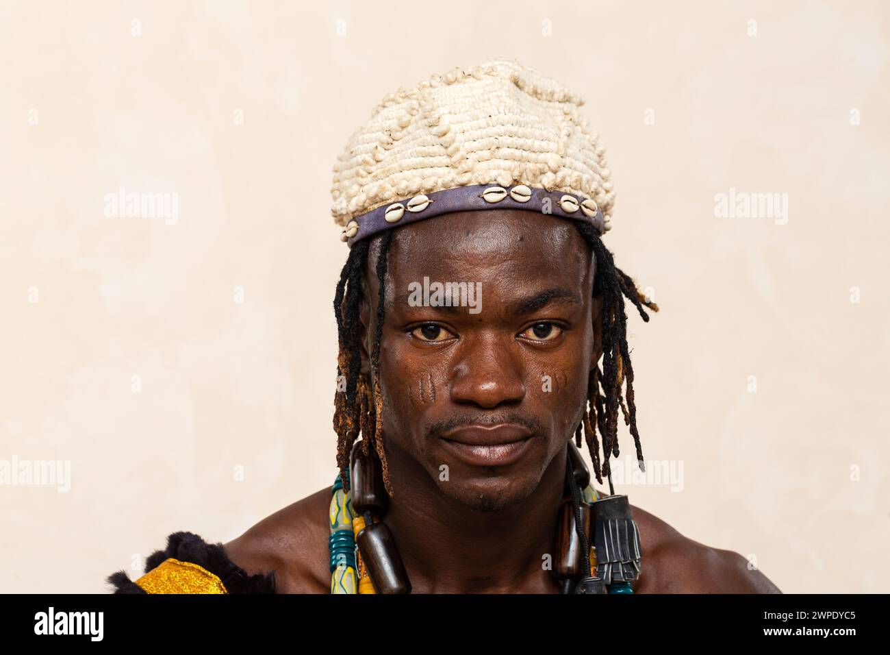 Nahaufnahme eines afrikanischen Mannes mit traditionellen Verzierungen, mit einem Stirnband aus Kaurischmuscheln und einer lebendigen Perlenkette, die seine widerspiegelt Stockfoto