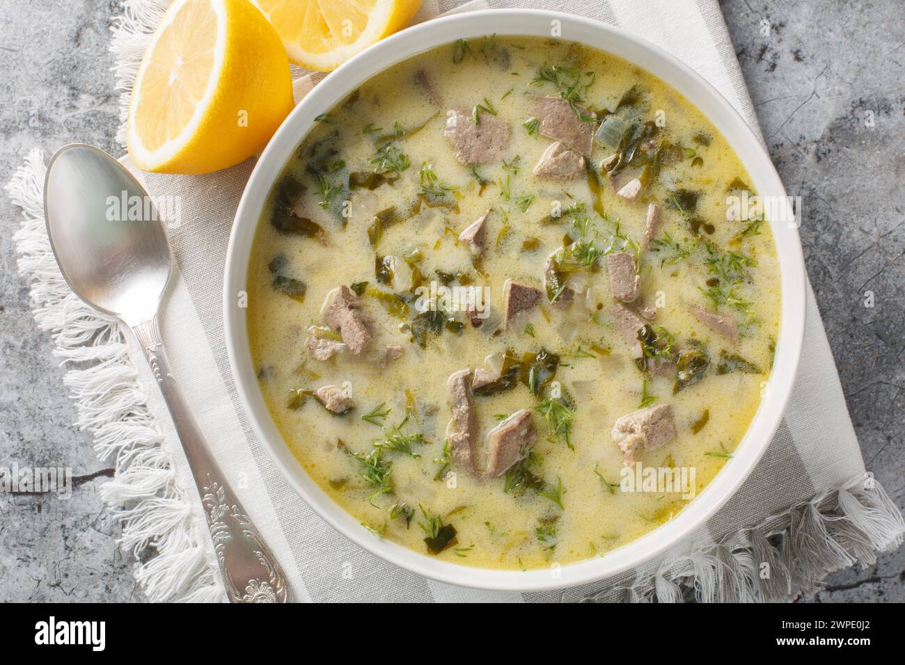 Griechische Ostersuppe mit Lammabfällen, Kräutern, gewürzt mit Ei und Zitronensauce in einer Schüssel auf einem Marmortisch. Horizontale Draufsicht von oben Stockfoto