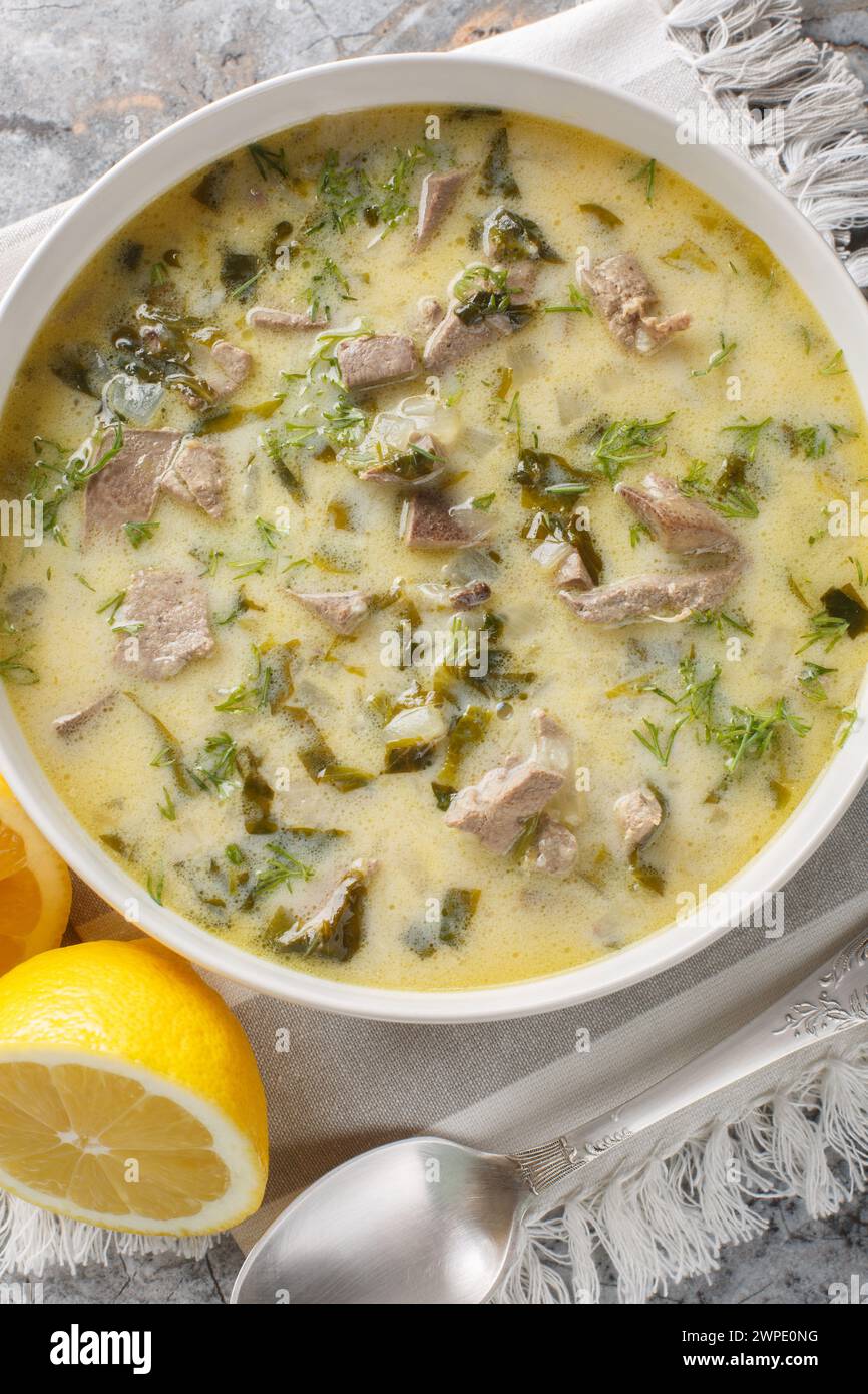 Griechische Ostersuppe Magiritsa mit Lammabfällen, Kräutern, mit Ei und Zitronensauce in einer Schüssel auf einem Marmortisch. Vertikale Draufsicht von abo Stockfoto