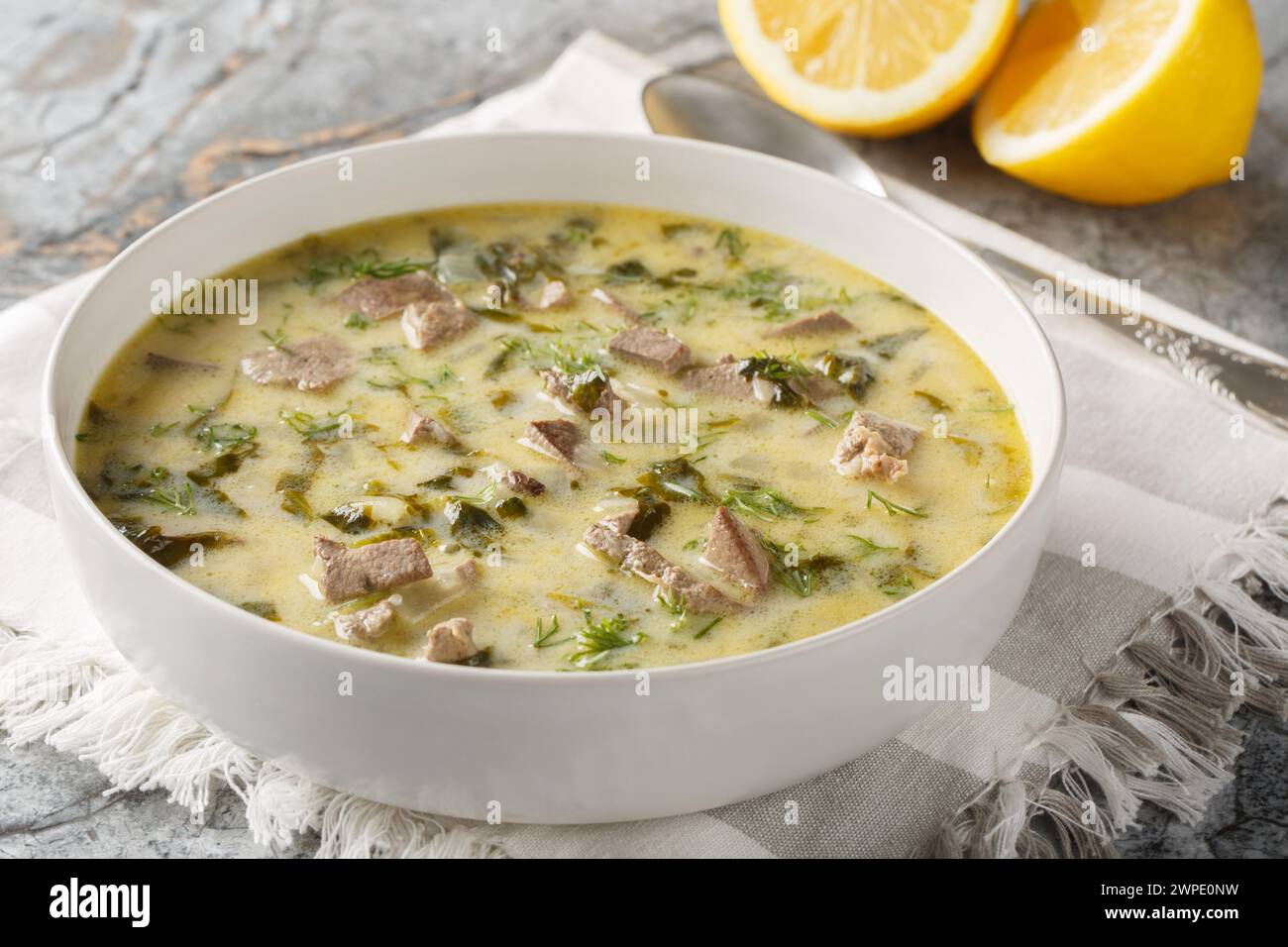 Griechische Ostersuppe mit Lammabfällen, Kräutern, gewürzt mit Ei und Zitronensauce in einer Schüssel auf einem Marmortisch. Horizontal Stockfoto