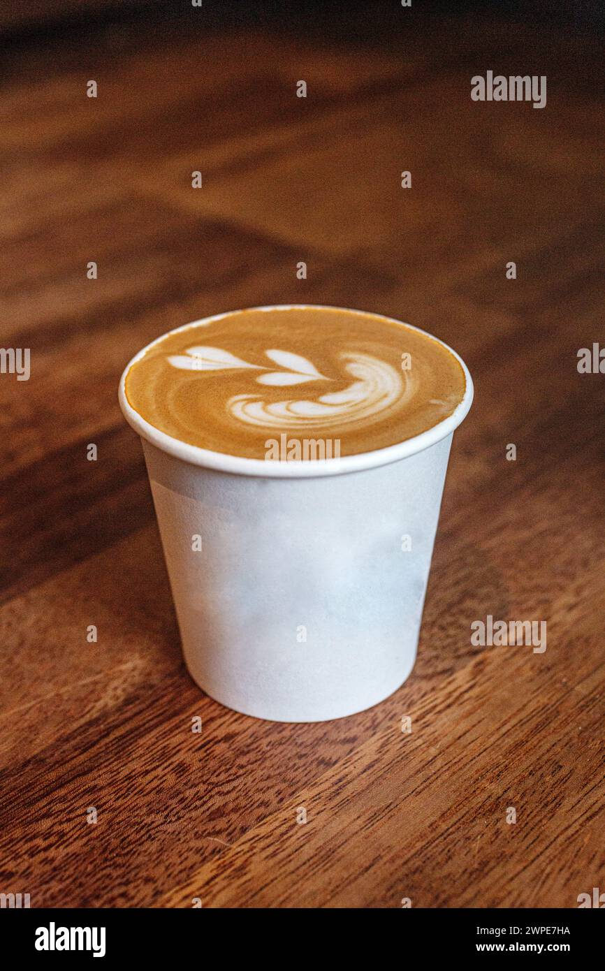 Nahaufnahme einer Tasse zum Mitnehmen mit herzförmiger Latte Art auf Holztafel Stockfoto