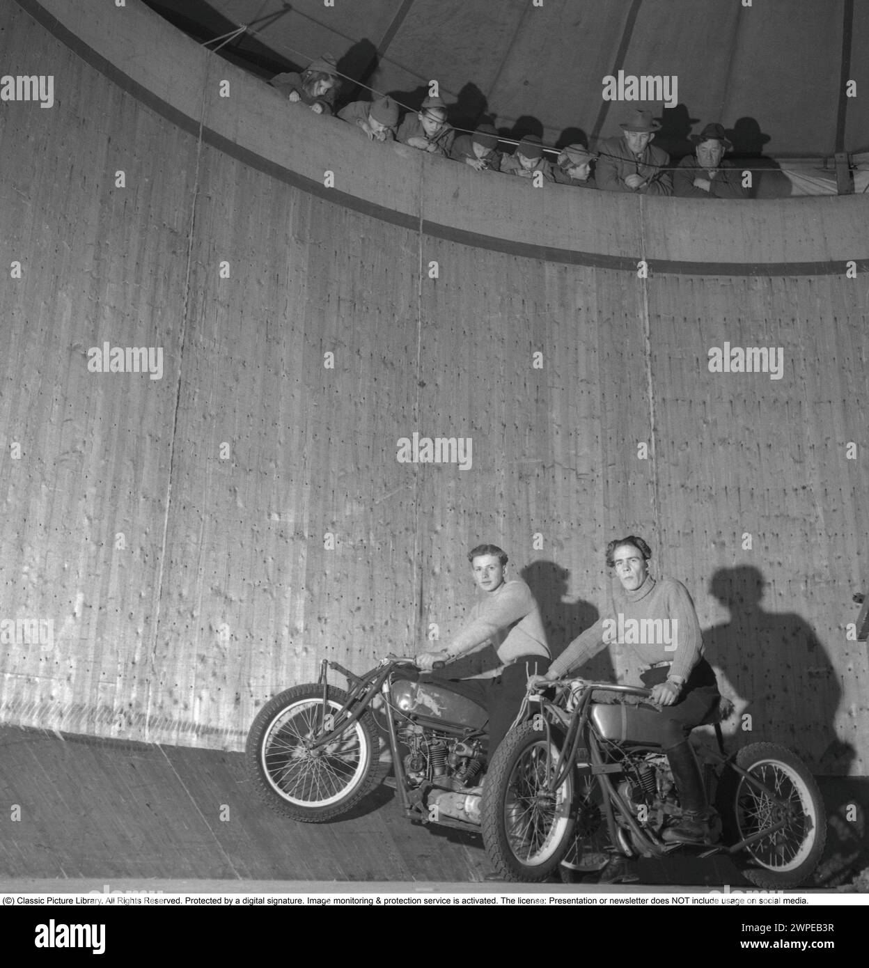 Mauer des Todes 1949. Die Mauer des Todes, das Motordrome, das Velodrome oder der Brunnen des Todes ist eine Nebenausstellung des Karnevals mit einem silos- oder tonnenförmigen Holzzylinder mit einem Durchmesser von normalerweise 6,1 bis 11,0 m (20 bis 36 Fuß) und aus Holzdielen, in der Motorradfahrer entlang der vertikalen Wand fahren und Stunts durchführen. durch Reibung und Zentrifugalkraft gehalten. Die ursprüngliche Mauer des Todes befand sich 1911 auf Coney Island in den Vereinigten Staaten. Ich habe mir einen Motorradfahrer in hoher Geschwindigkeit im Velodrome vorgestellt, der mit den Händen in der Luft zeigte, nicht wie er sollte am Lenker. Schweden 1947. Conard Stockfoto