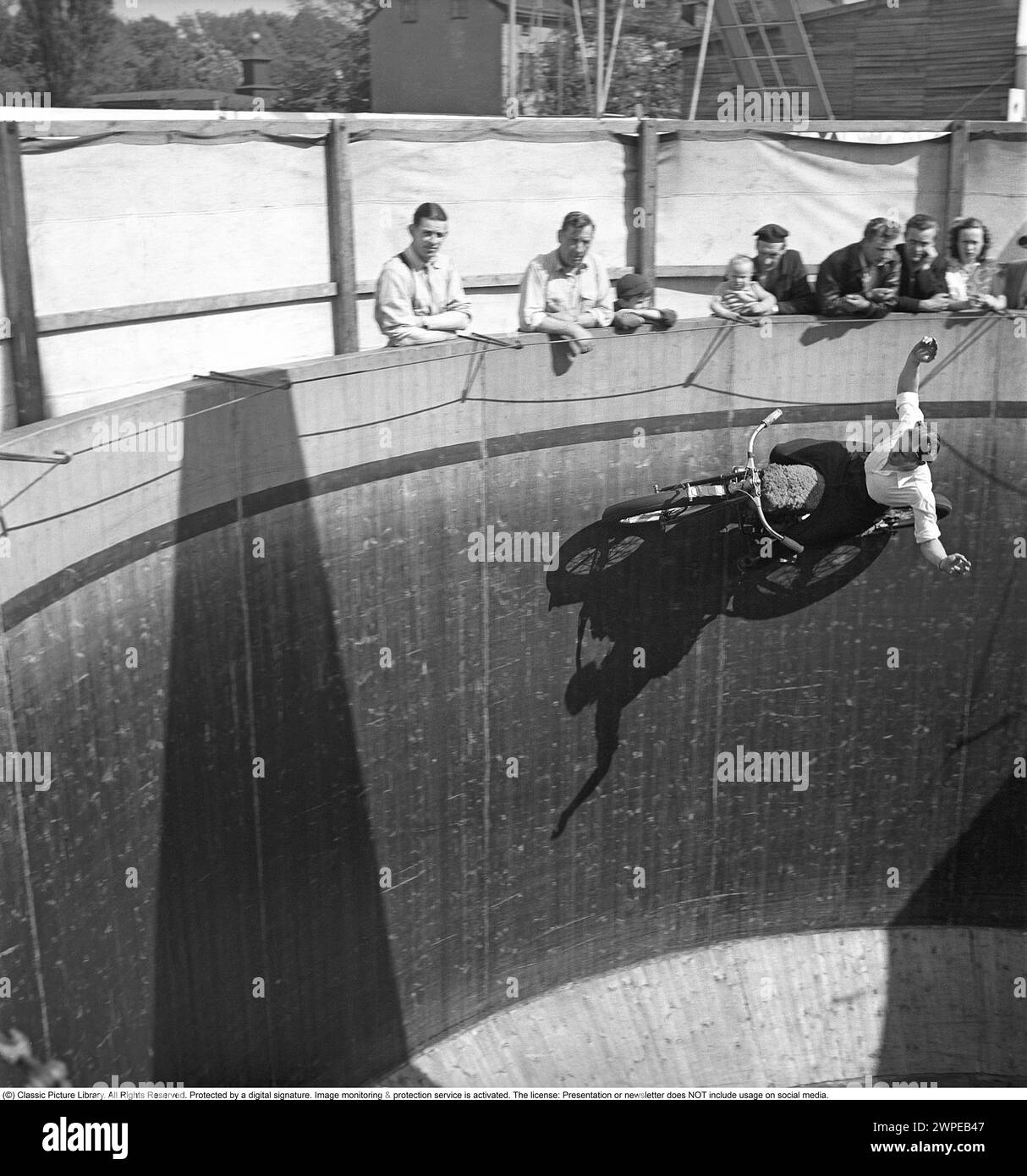 Mauer des Todes 1949. Die Mauer des Todes, das Motordrome, das Velodrome oder der Brunnen des Todes ist eine Nebenausstellung des Karnevals mit einem silos- oder tonnenförmigen Holzzylinder mit einem Durchmesser von normalerweise 6,1 bis 11,0 m (20 bis 36 Fuß) und aus Holzdielen, in der Motorradfahrer entlang der vertikalen Wand fahren und Stunts durchführen. durch Reibung und Zentrifugalkraft gehalten. Die ursprüngliche Mauer des Todes befand sich 1911 auf Coney Island in den Vereinigten Staaten. Ich habe mir einen Motorradfahrer in hoher Geschwindigkeit im Velodrome vorgestellt, der mit den Händen in der Luft zeigte, nicht wie er sollte am Lenker. Schweden 1949. Conard Stockfoto