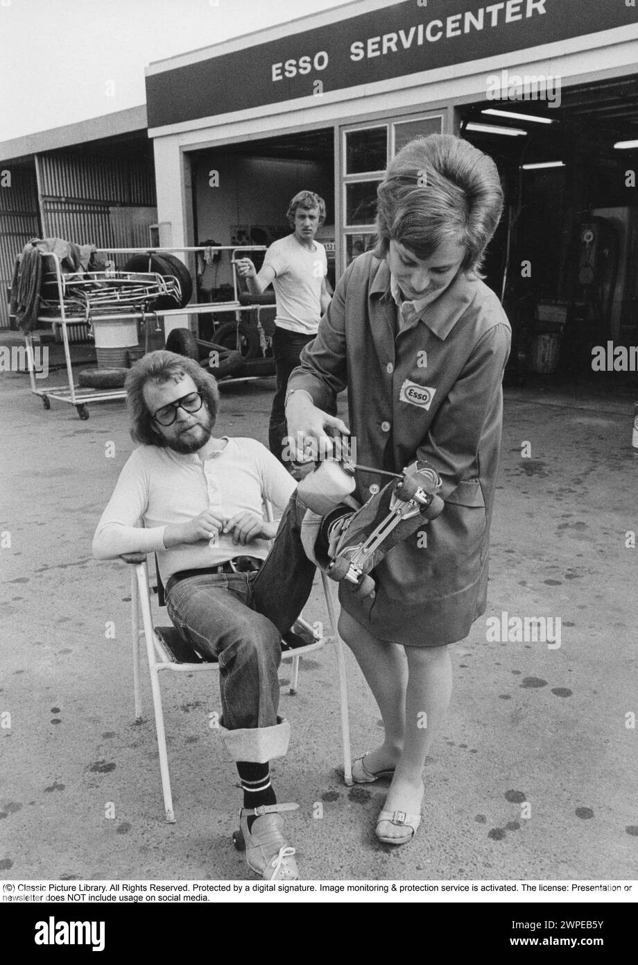 Rollschuhe 1972. Ein Mann auf Rollschuhen wird an einer Esso-Tankstelle gesehen, wie seine Räder geschmiert werden. Eine Frau des Personals wird mit einer Ölkanne gesehen, die die Räder schmiert. Schweden 1972. Stockfoto