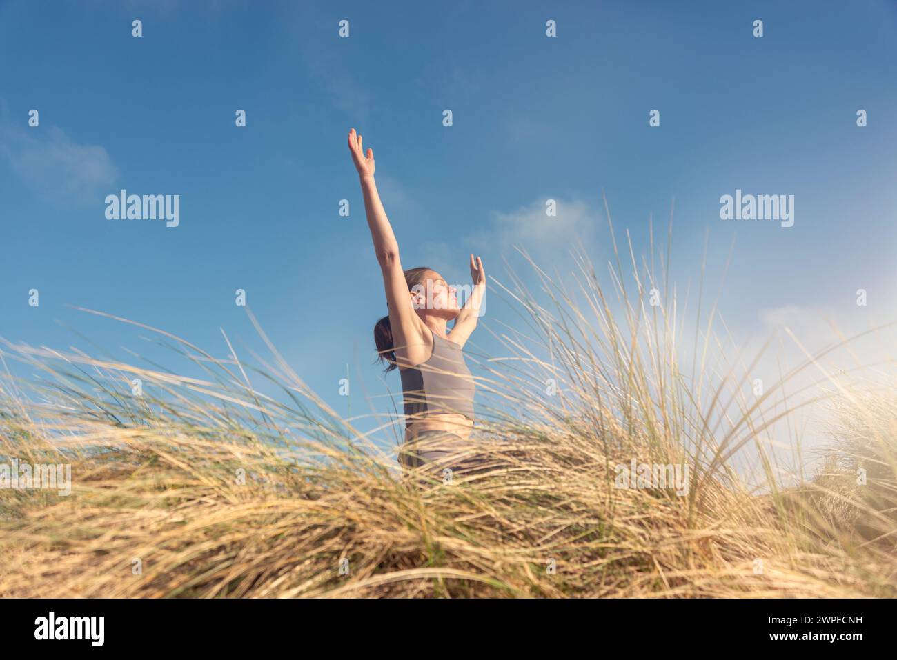 Sportliche Frau mit erhobenen Armen und Blick zur Sonne, Stockfoto