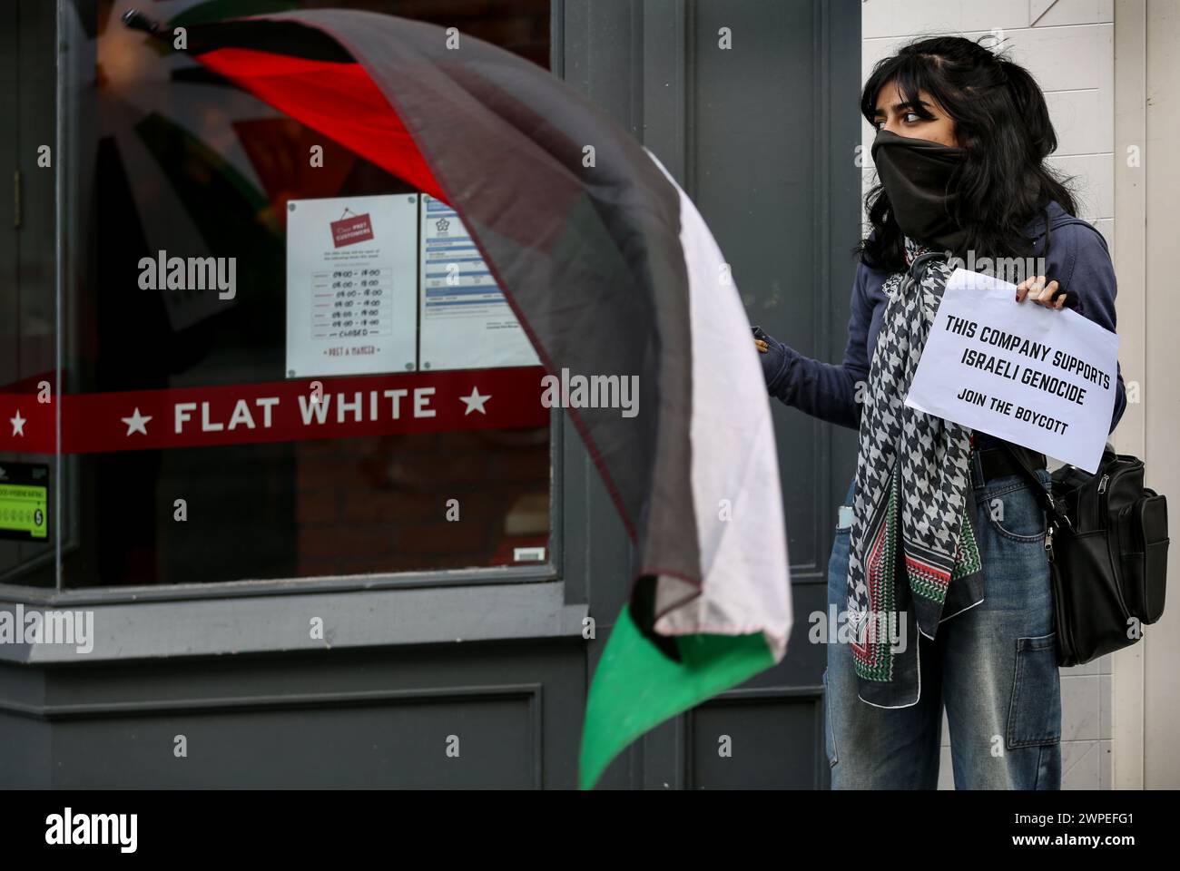 Ein Demonstrant steht vor Pret A Krippe mit einer palästinensischen Flagge und einem Plakat mit der Aufschrift "diese Kompanie unterstützt den israelischen Völkermord, tritt dem Boykott bei" während einer Demonstration. Demonstranten fordern, dass die Leute Costa Coffee boykottieren. Ihre Muttergesellschaft Coca-Cola betreibt eine Fabrik in der illegalen israelischen Siedlung Atarot in dem Gebiet, das von den Demonstranten als Palästina besetzt angesehen wird. Die Boykott Divestment and Sanctions (BDS)-Bewegung arbeitet daran, die internationale Unterstützung für Israels Unterdrückung der Palästinenser zu beenden und Israel unter Druck zu setzen, sich an das Völkerrecht zu halten, und hat eine Liste von Unternehmen zusammengestellt Stockfoto