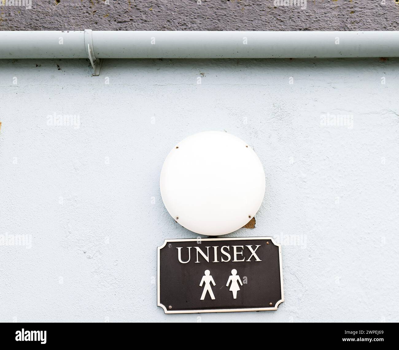 Unisex-WC-Schild in schwarz auf weißem Grund unter kreisförmigem Licht mit Dachrinne oben Stockfoto