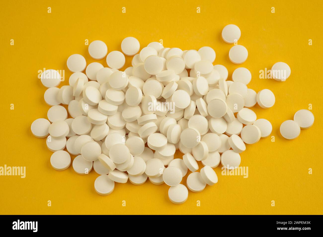 Nahaufnahme von oben eines Stapels weißer, runder Vitamin-D-Tabletten, der lose auf gelbem Hintergrund liegt Stockfoto
