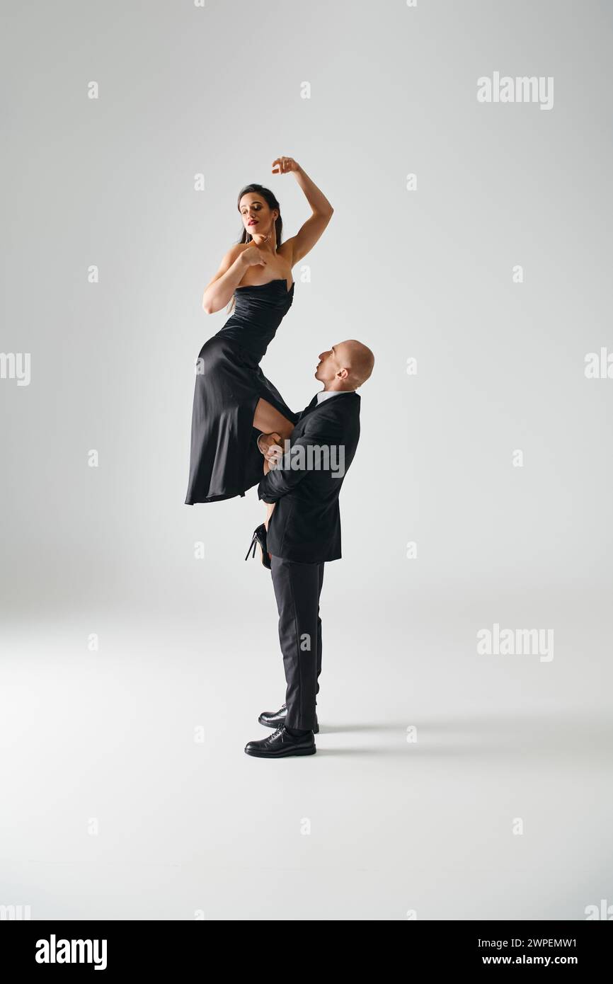 Mann hebt junge elegante Frau in schwarzem Kleid und High Heels, die während der Performance ausbalancieren Stockfoto