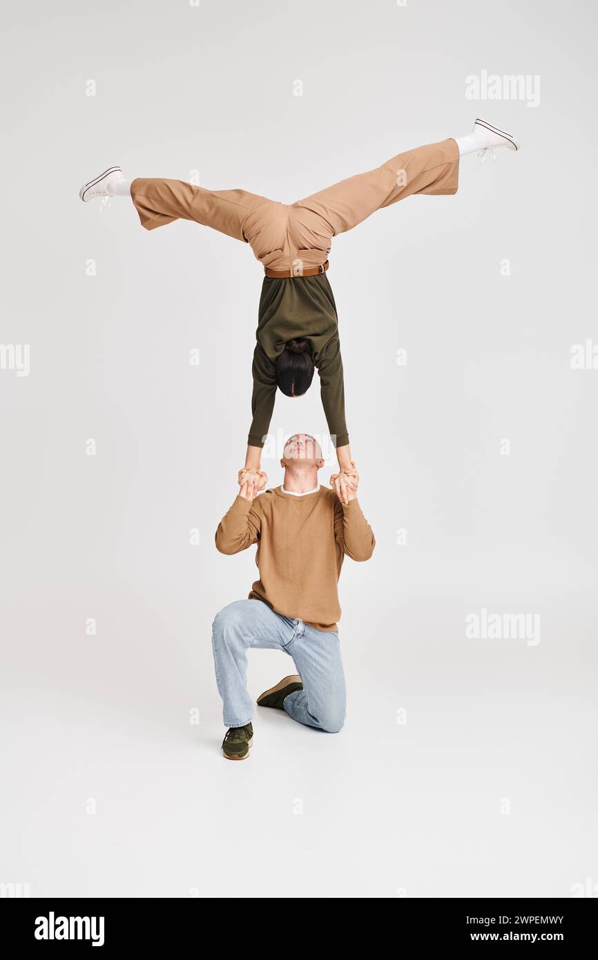 Verspieltes akrobat-Duo mit Frau im Kopfstand, unterstützt von kniendem Mann im Studio auf grauem Hintergrund Stockfoto Verspieltes akrobat-Duo mit Frau im Kopfstand, unterstützt von kniendem Mann im Studio auf grauem Hintergrund Stockfoto
