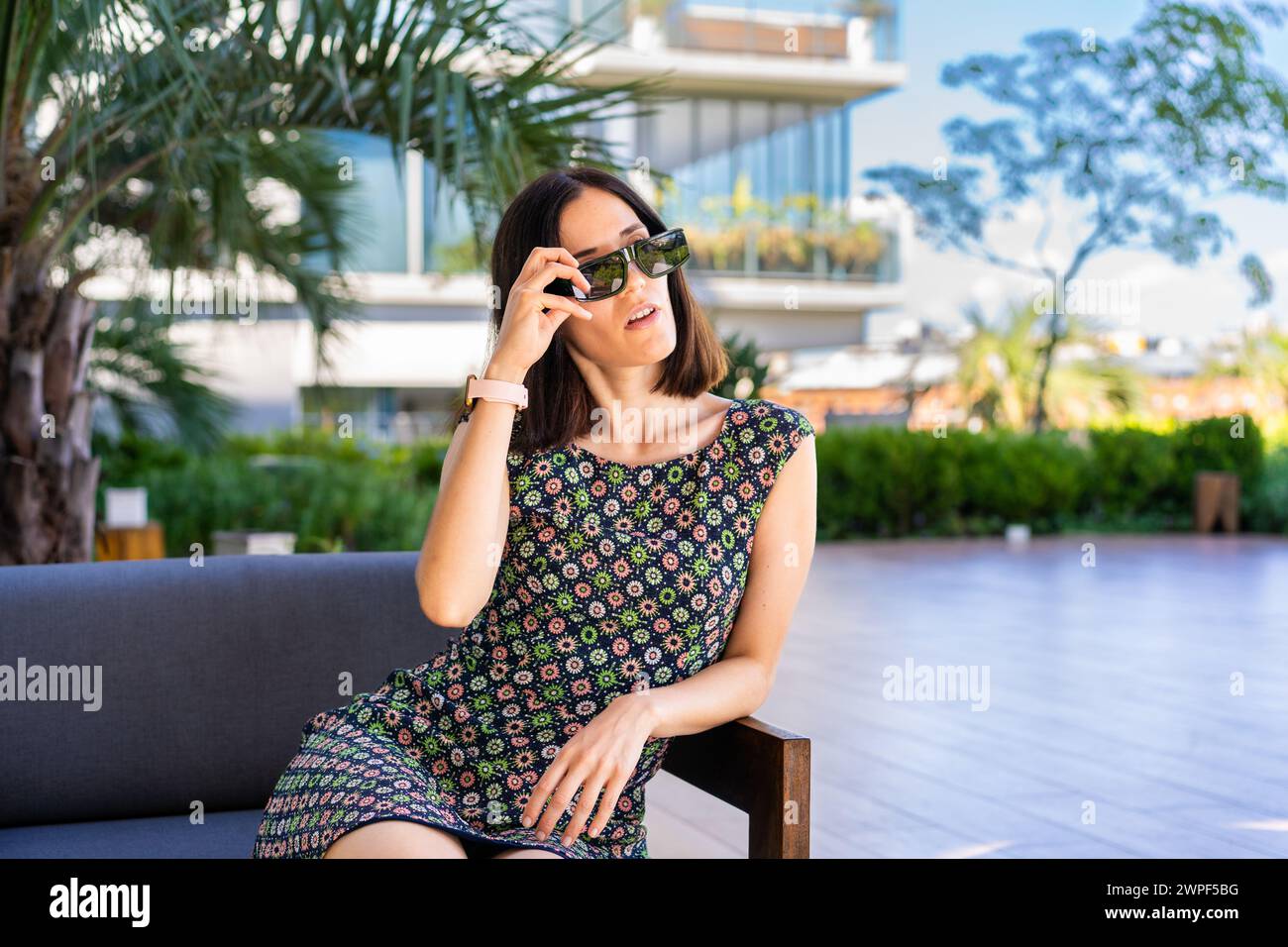 Eine schöne Frau sitzt draußen auf einer Couch, während sie ihre Sonnenbrille auszieht. Stockfoto