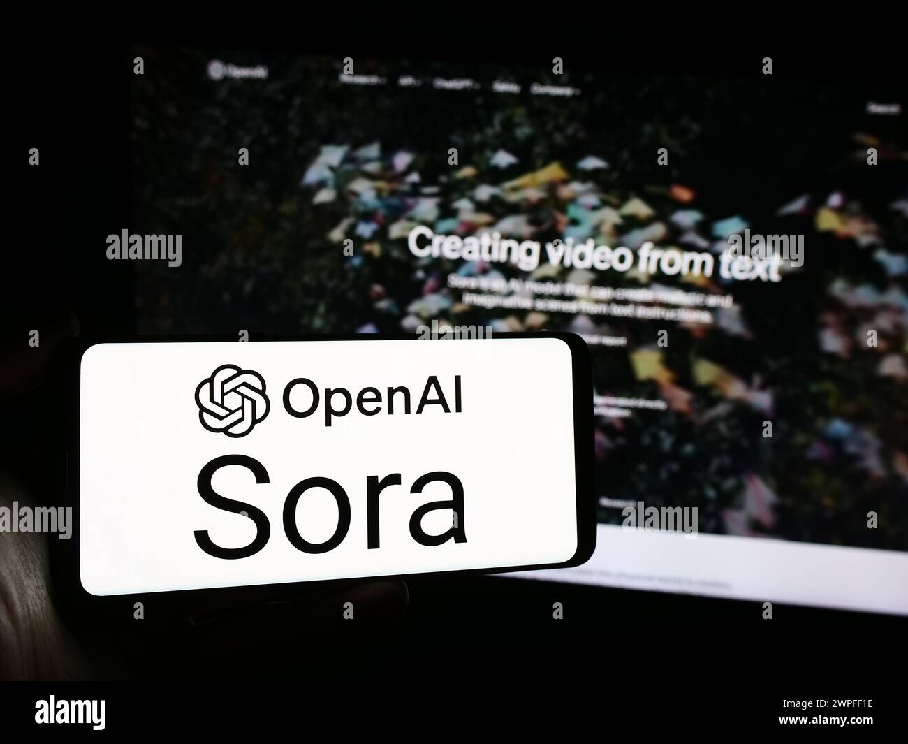 Person mit Smartphone und Logo der Text-to-Video-Modellsoftware Sora (OpenAI) vor der Website. Schwerpunkt auf dem Display des Telefons. Stockfoto