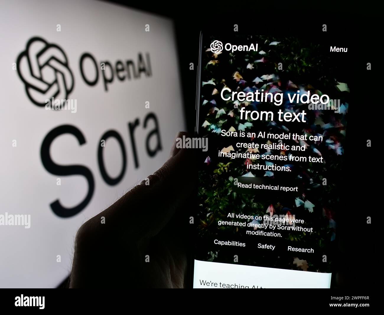 Person, die ein Mobiltelefon hält und vor dem Logo eine Webseite der Text-to-Video-Modellsoftware Sora (OpenAI) zeigt. Konzentrieren Sie sich auf die Mitte des Telefondisplays. Stockfoto