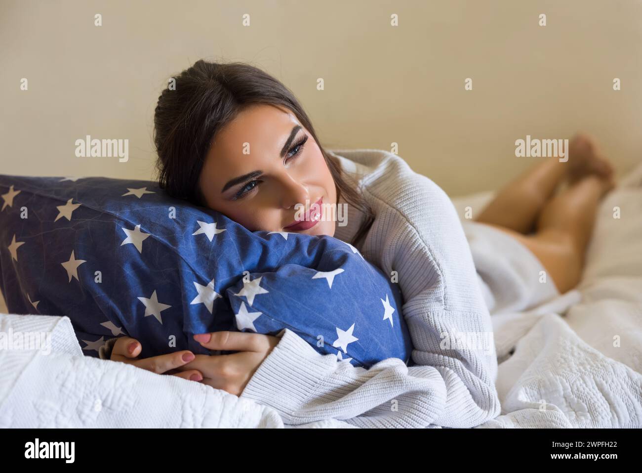 Schöne junge Frau trägt einen weißen groben Pullover und entspannt sich im Bett Stockfoto