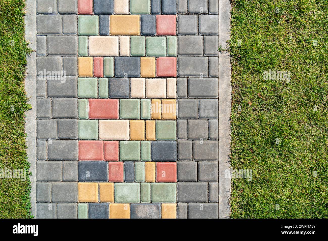 Farbenfrohe gepflasterte Straße über üppigen Rasen an sonnigen Tagen. Weg mit hellen Stufensteinen im Sommerpark. Kreatives Designelement der Landschaftsgestaltung von oben Stockfoto