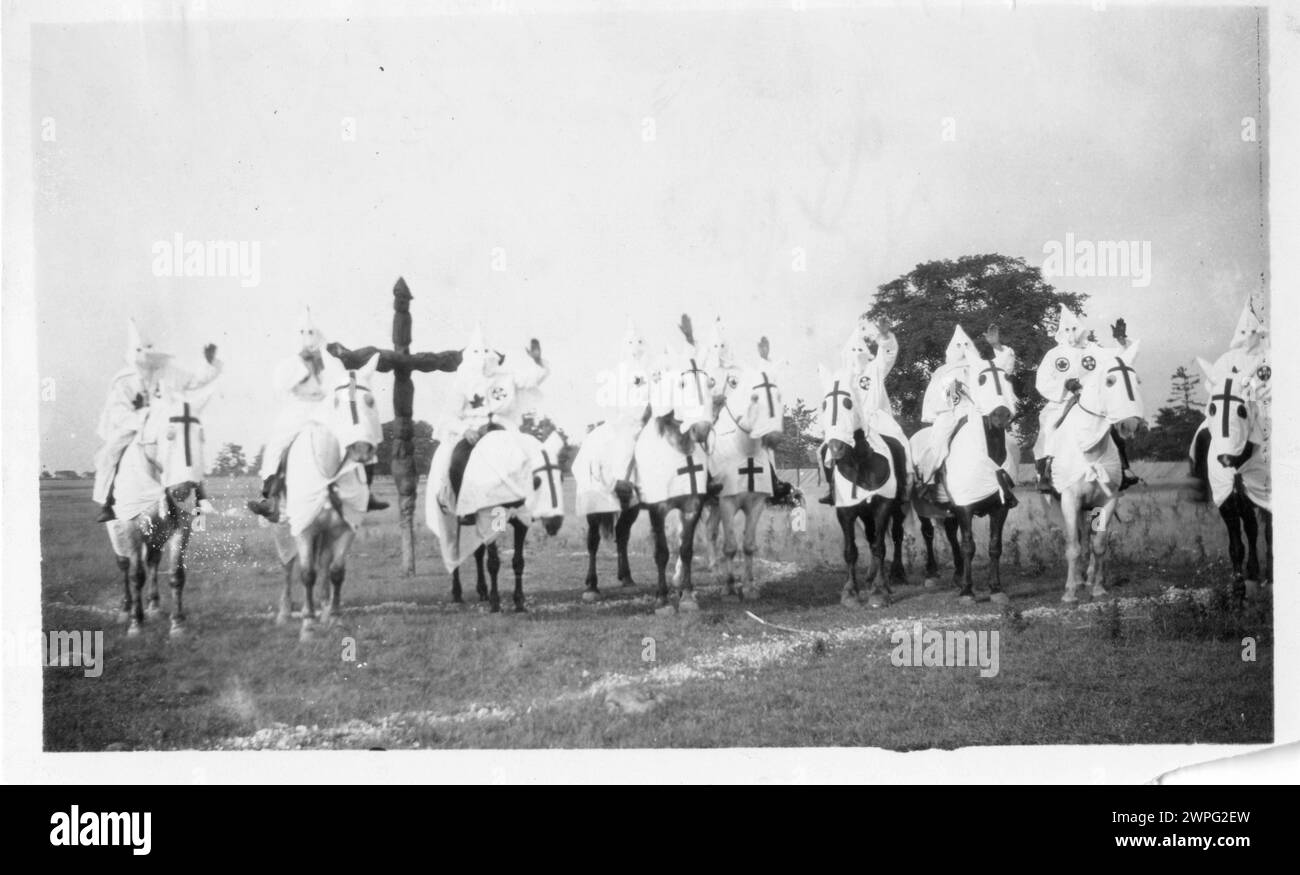 Historisches Vintage-Foto. Mitglieder des Ku Klux Klan sitzen auf Kapuzenpferden neben einem Kreuz in der Nähe von Belleville, Ontario. Ihre linken Hände sind hoch. .Kanada um 1927 Stockfoto