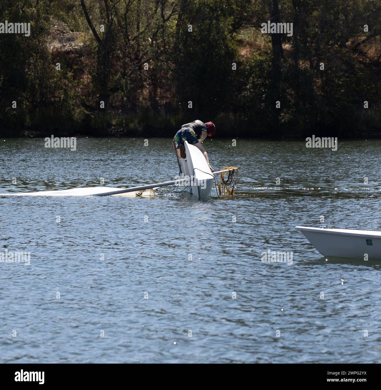 Ein junges Mädchen lernte, im See zu segeln, kippte aber über ihr Wasserfahrzeug und versuchte, ihr Boot zu korrigieren, indem es mit Algen auf ihrem Segelboot lag. Stockfoto