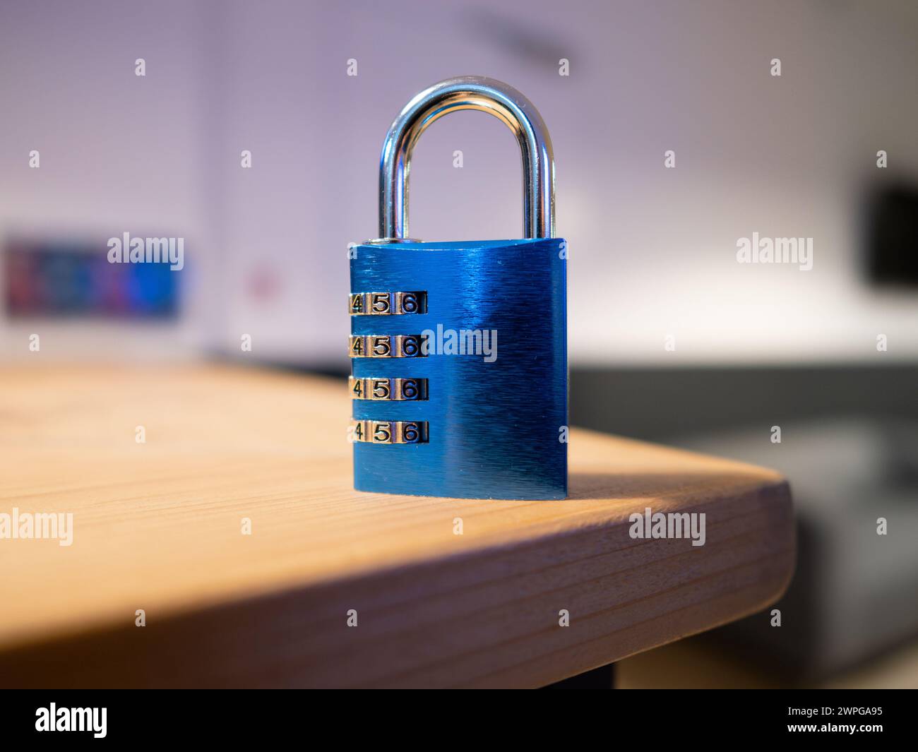 Kombinationsschloss in blauer Farbe auf einem Holztisch. Geschlossenes Vorhängeschloss mit 4 Zahlenreihen zum Einstellen eines Codes. Symbol eines verschlossenen Geheimnisses. Stockfoto