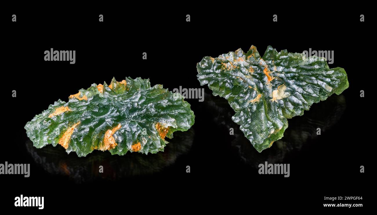 Seltene Tektitminerale Moldaviten mit Orangenflecken auf grüner faltiger Oberfläche. Rohe ungeschnittene Edelsteine aus Meteoritenglas und Reflexion auf schwarzem Hintergrund. Stockfoto