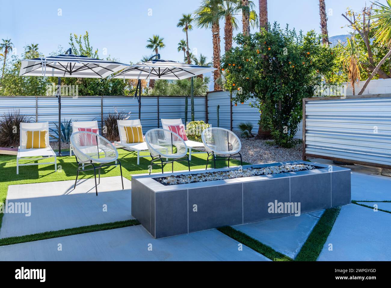Liegestühle im Hinterhof mit Sonnenschirmen, farbenfrohen Kissen und einem Kamin in Palm Springs, Kalifornien Stockfoto