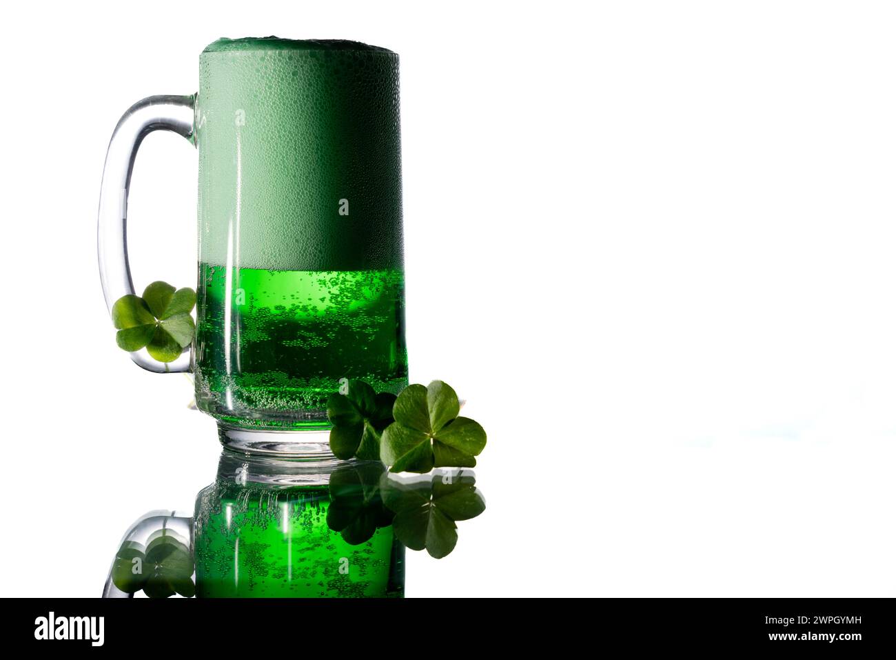 Grünes Getränk in einem clair Glas neben Klee auf einem Glastisch mit Kopierraum rechts. Stockfoto