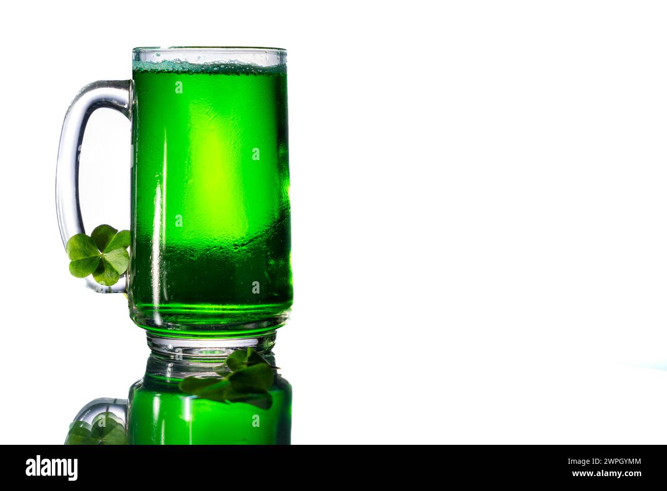 Grünes Getränk in einem clair Glas neben Klee auf einem Glastisch mit Kopierraum rechts. Stockfoto