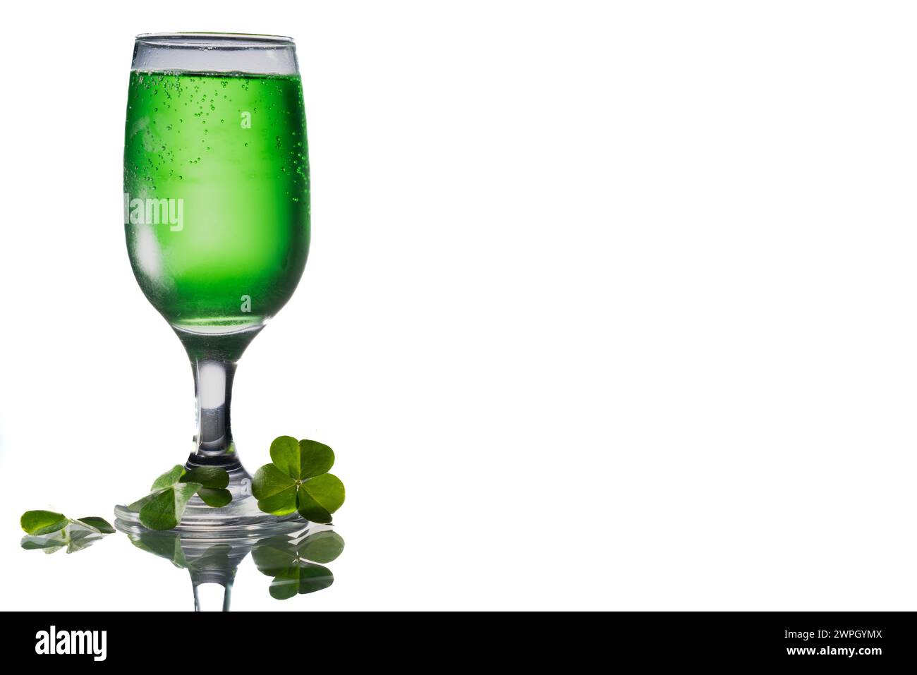 Grünes Getränk in einem clair Glas neben Klee auf einem Glastisch mit Kopierraum rechts. Stockfoto