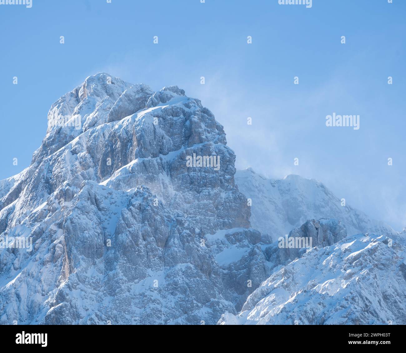 Schneebedeckter, sonnendurchfluteter Gipfel im Krnica-Tal, den Julischen Alpen an einem klaren Wintertag. Der Wind wehte Schnee vom Gipfel. Stockfoto