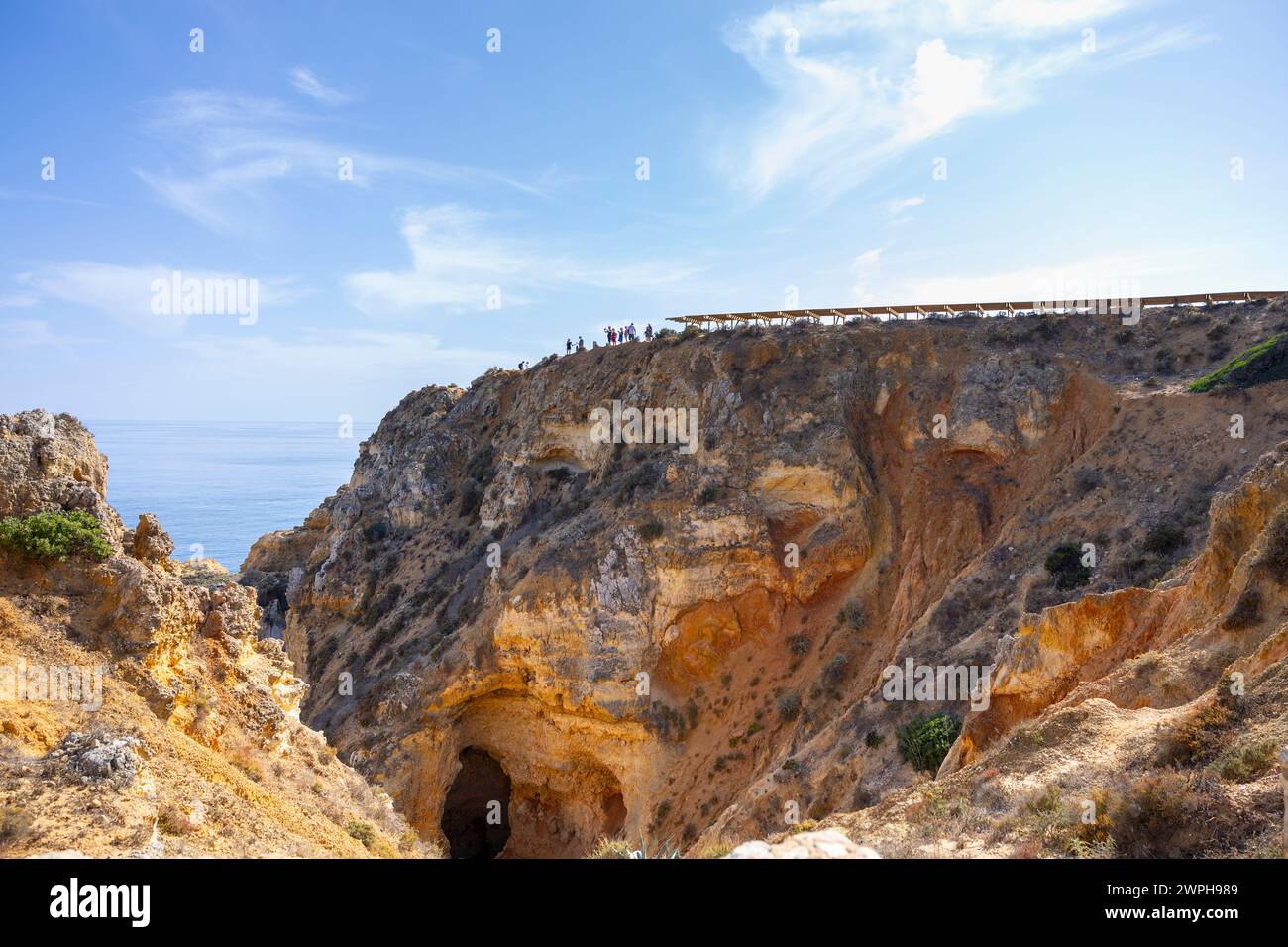 Große Felsformation mit oben dem Aussichtspunkt mit Touristen, die die Landschaft in Ponta da Piedade, Lagos, Algarve, Portugal betrachten Stockfoto