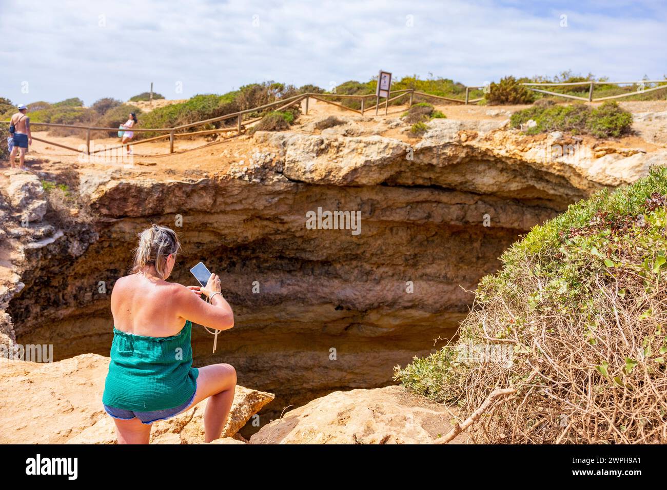 Junge Frau, die ein Foto in die Benagil-Höhle macht, während sie auf einer Klippe steht. Benagil, Carvoeiro, Algarve, Portugal. Stockfoto