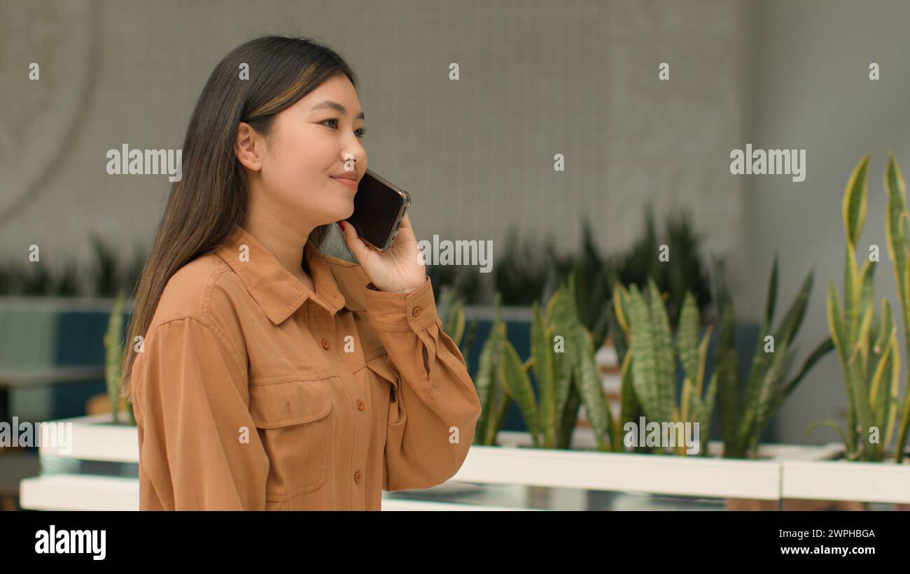 Seitenansicht Asiatische Geschäftsfrau lächelnd chinesische koreanisch japanische Frau Angestellte Manager gehen im Business Center sprechen Handy verhandeln Stockfoto