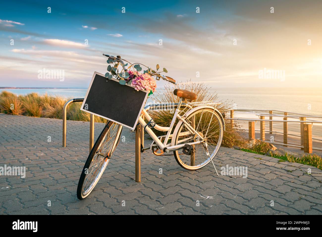 Vintage-Fahrrad mit Textbannerrahmen auf einem Lenkrad, das bei Sonnenuntergang in der Nähe des Strandes geparkt ist Stockfoto