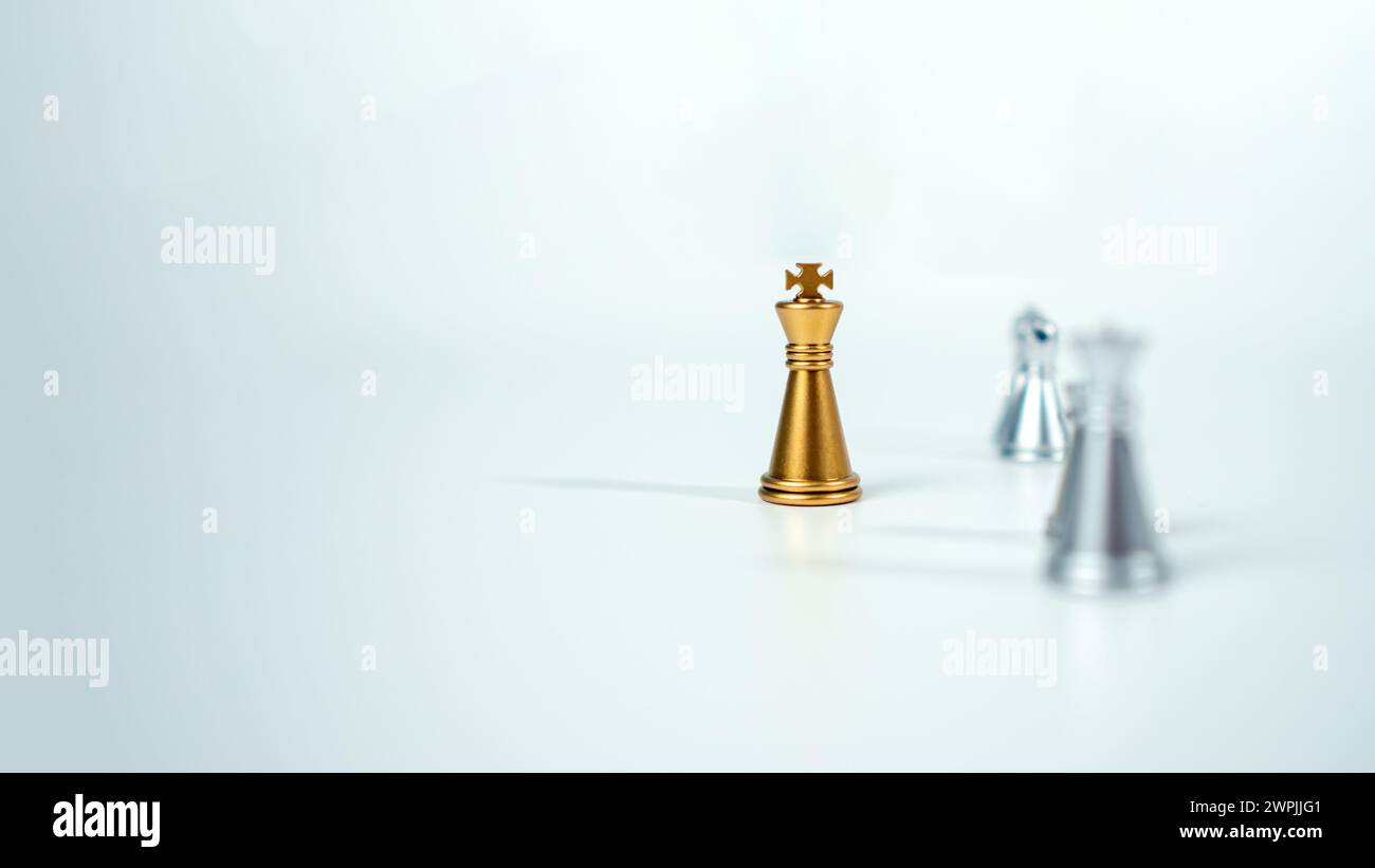 Goldenes Königsschach auf dem Brett vor silbernen Schachstücken auf weißem Hintergrund mit Kopierraum, Führung, Kämpfer, Geschäftsführung, Wettbewerb Stockfoto