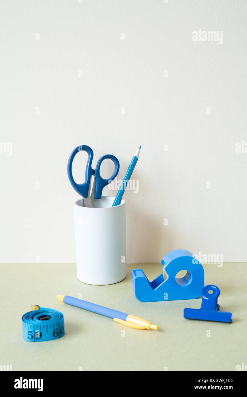Blaue Schreibwaren. Farbstift, Stift, Schere, Clip, Bandmaß, Klebebandspender auf dem Schreibtisch. Weißer elfenbeinfarbener Hintergrund Stockfoto