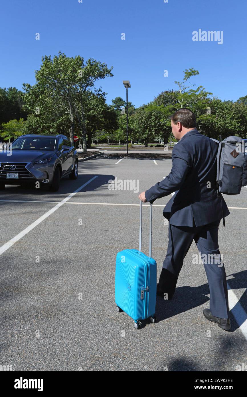 Seitenansicht eines männlichen Geschäftsreisenden, der seinen Koffer zum Auto rollte. Stockfoto