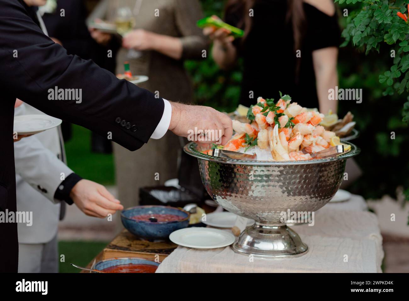 Gäste in Anzügen an der Rezeption, die nach Shrimps-Vorspeisen greifen Stockfoto