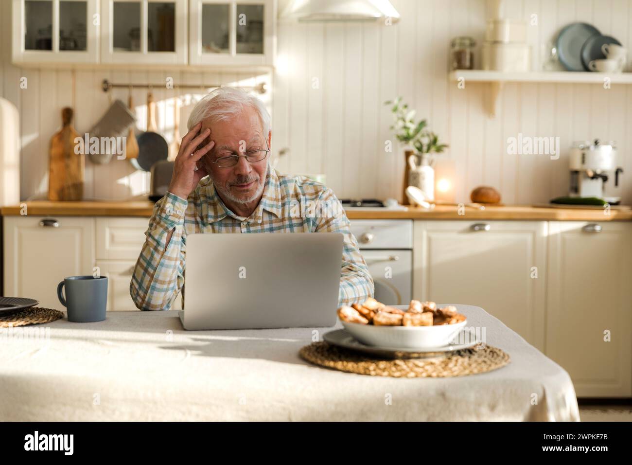 Älterer grauhaariger Mann mit Brille versucht, allein mit dem Laptop umzugehen Stockfoto