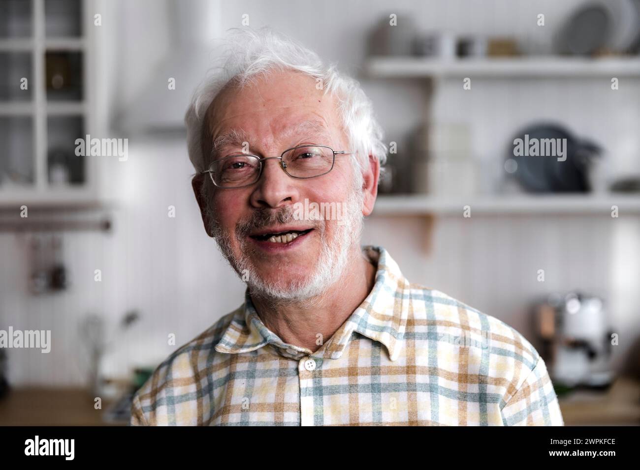 Porträt eines älteren, fröhlichen Mannes, der in der gemütlichen Küche steht und lächelt Stockfoto