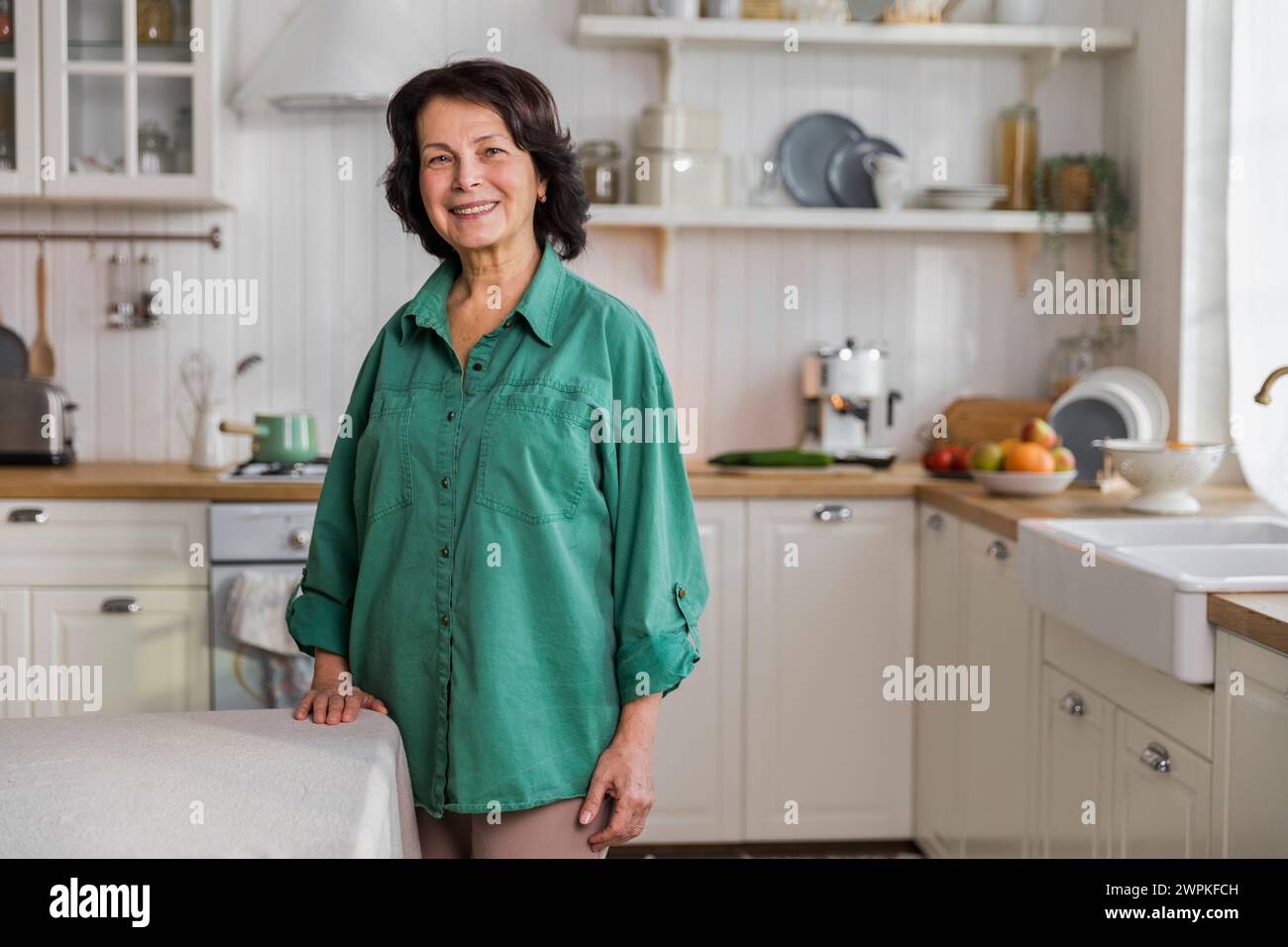 Porträt einer älteren, fröhlichen Frau, die in der gemütlichen Küche steht Stockfoto