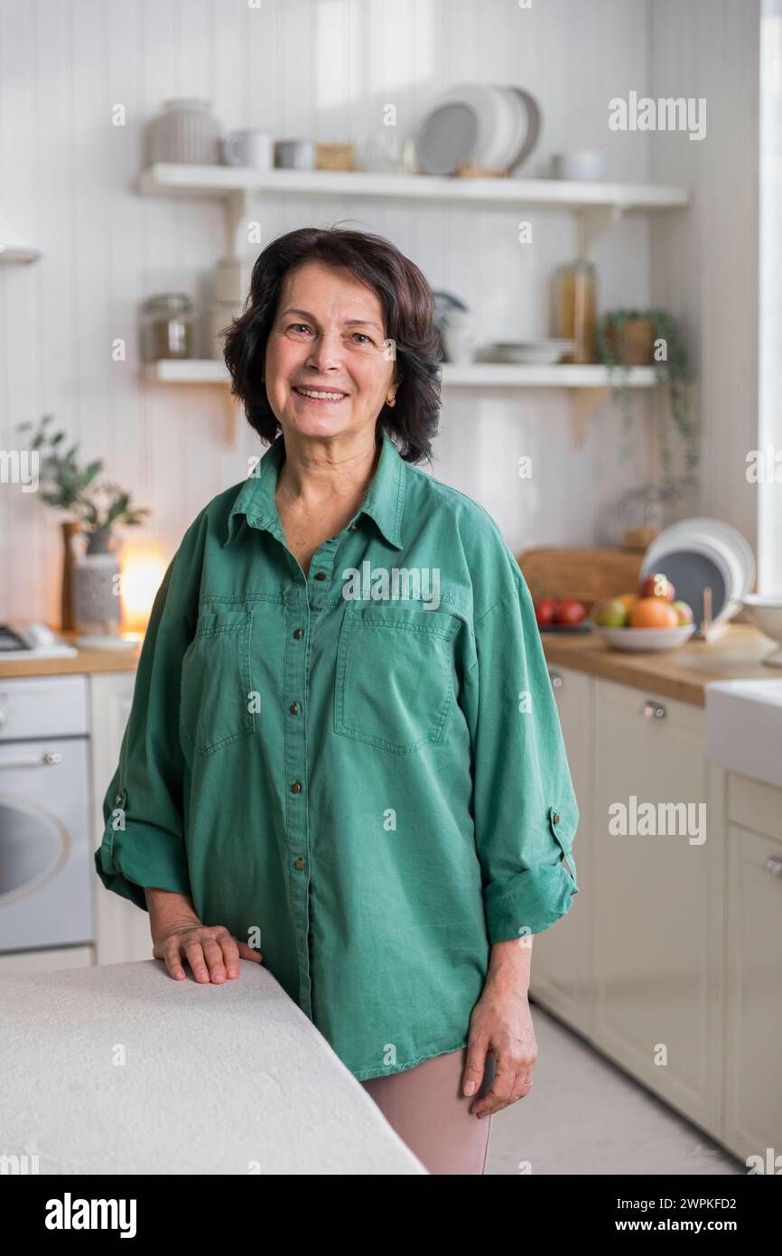 Porträt einer älteren, fröhlichen Frau, die in der gemütlichen Küche steht Stockfoto