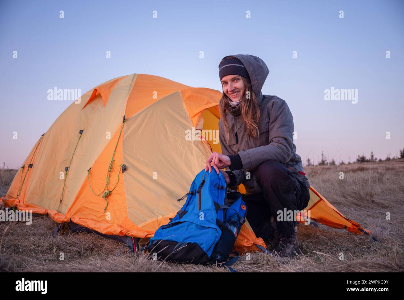 Lächelnde Frau öffnet Rucksack am Zelt in den Bergen Stockfoto
