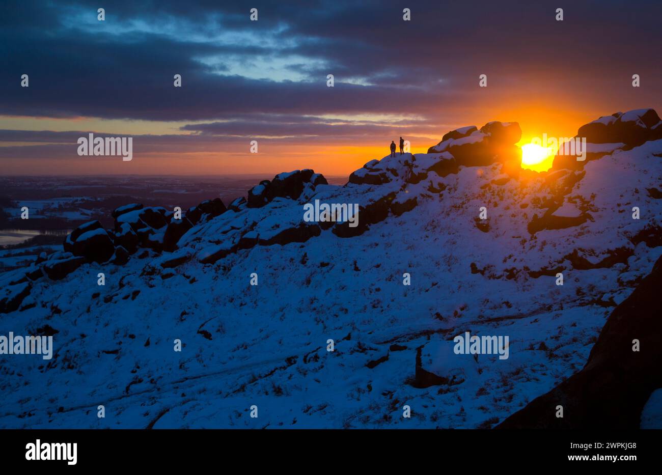 02/15 ohne Ende der Eiszeit, die das Land packt, stehen zwei Bergsteiger auf Felsen, um einen beeindruckenden Sonnenuntergang zu bestaunen Stockfoto