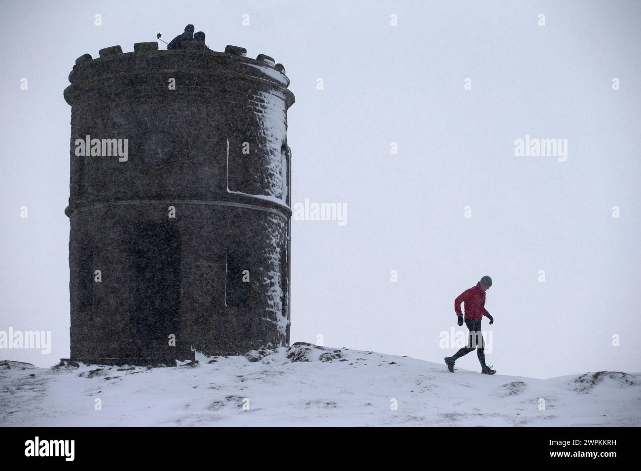 21/02/15 nach starken Schneeschauern über dem Derbyshire Peak District trotzt ein einsamer Läufer der Kälte im Solomon's Temple, auch bekannt als Grinlow Tow Stockfoto