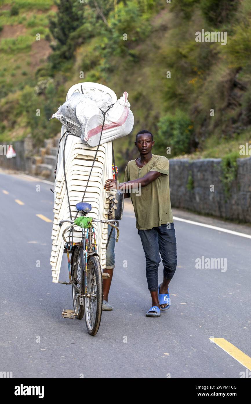 Mann schiebt eine Ladung Plastikstühle auf ein Fahrrad in Westruanda, Afrika Stockfoto