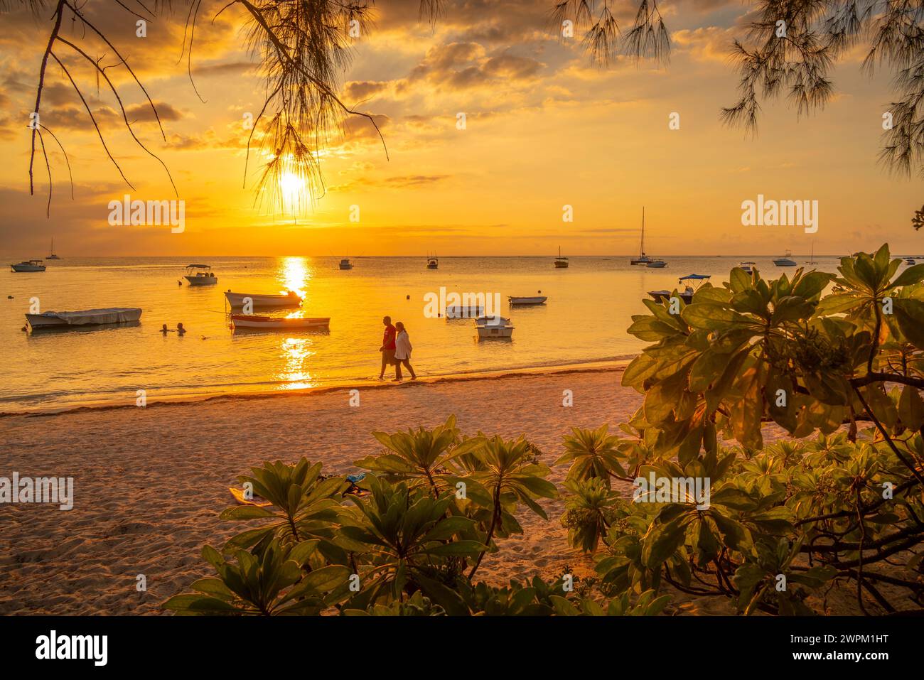 Blick auf Boote und Menschen am öffentlichen Strand Mon Choisy bei Sonnenuntergang, Mauritius, Indischer Ozean, Afrika Stockfoto